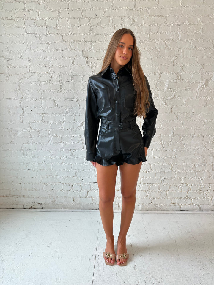 Woman wearing black leather long sleeve romper with ruffle hem.