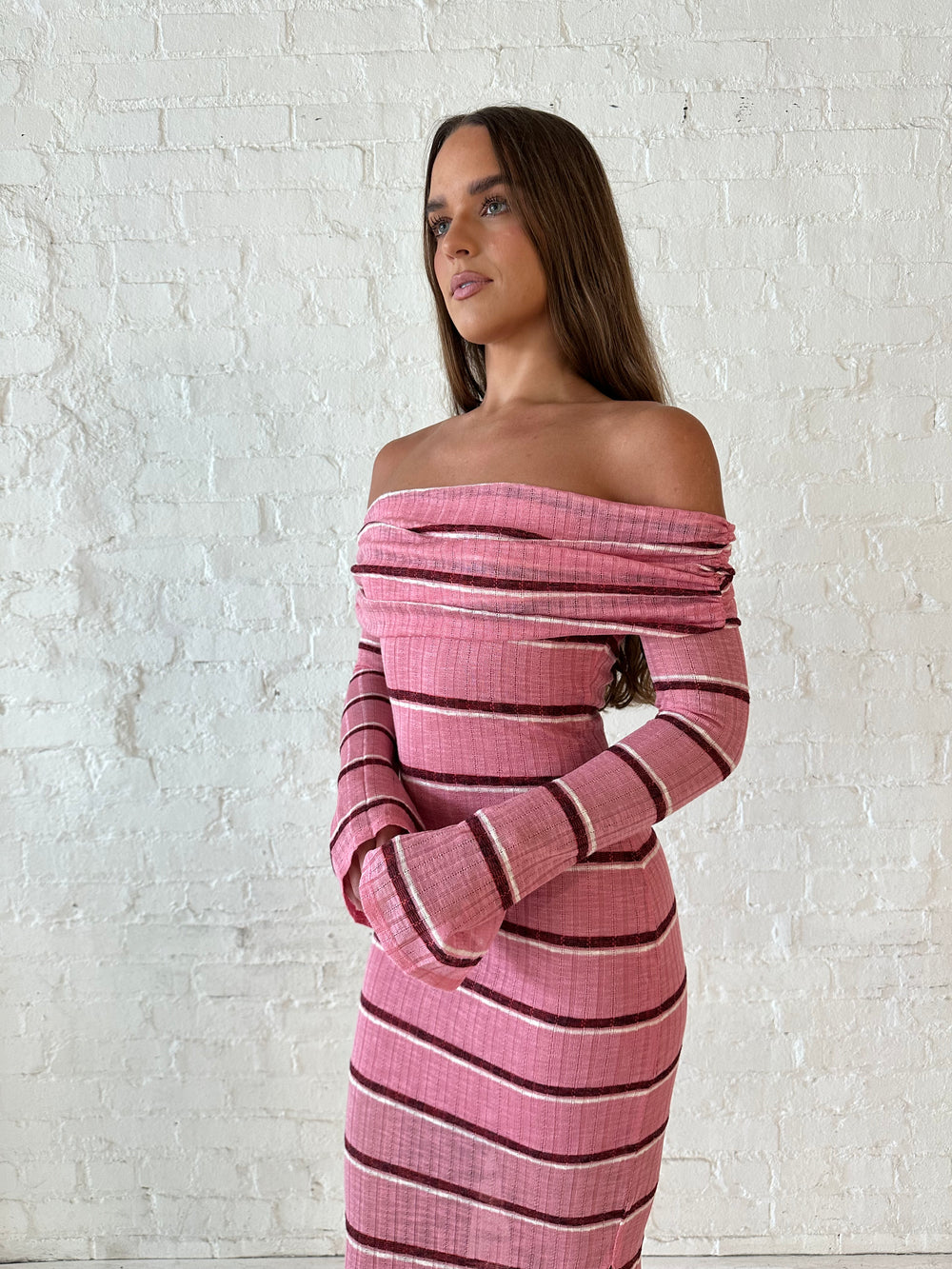 Woman wearing a pink maxi dress with burgundy stripes, fold over off the shoulder neckline, and long sleeves. 