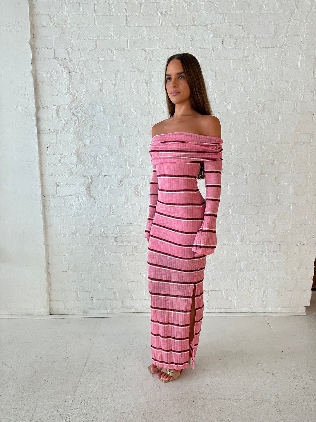 Woman wearing a pink maxi dress with burgundy stripes, fold over off the shoulder neckline, and long sleeves. 