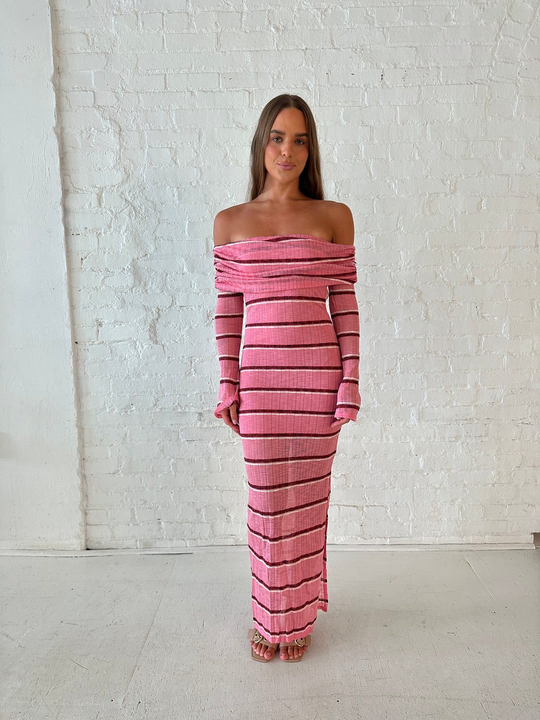Woman wearing a pink maxi dress with burgundy stripes, fold over off the shoulder neckline, and long sleeves. 