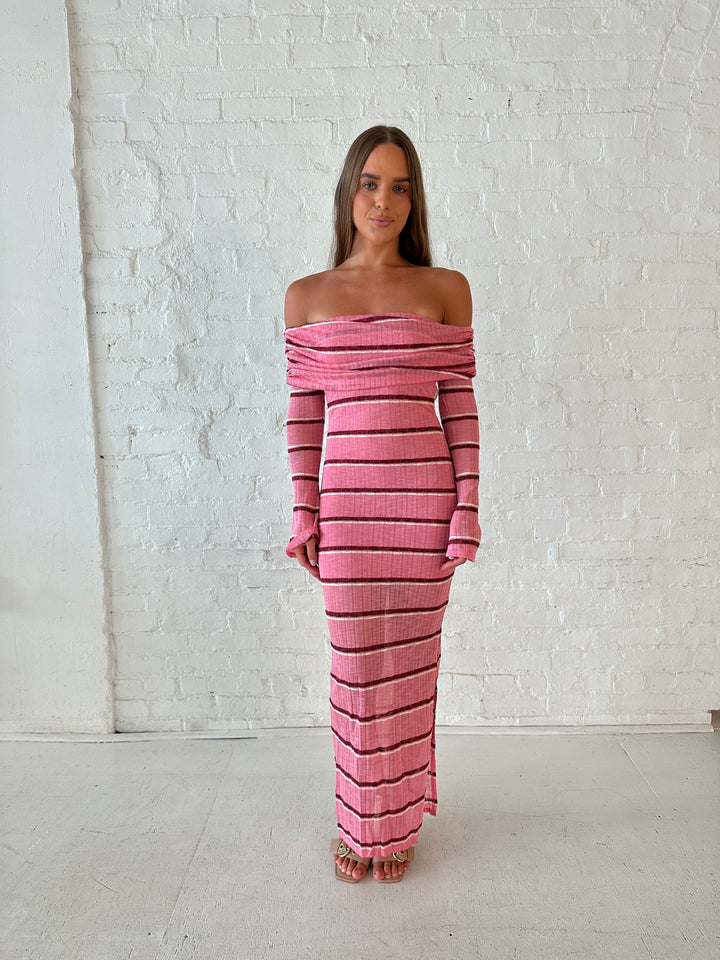 Woman wearing a pink maxi dress with burgundy stripes, fold over off the shoulder neckline, and long sleeves. 