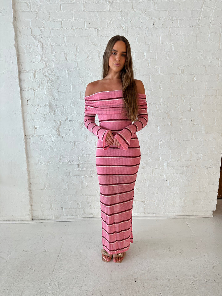 Woman wearing a pink maxi dress with burgundy stripes, fold over off the shoulder neckline, and long sleeves. 