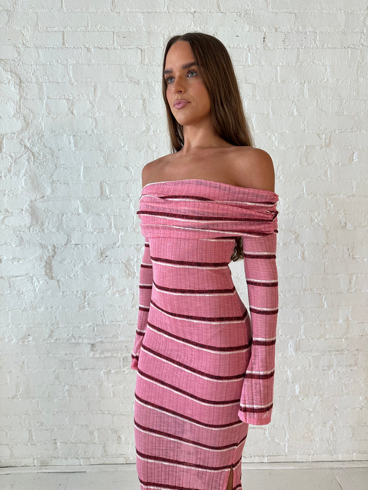 Woman wearing a pink maxi dress with burgundy stripes, fold over off the shoulder neckline, and long sleeves. 