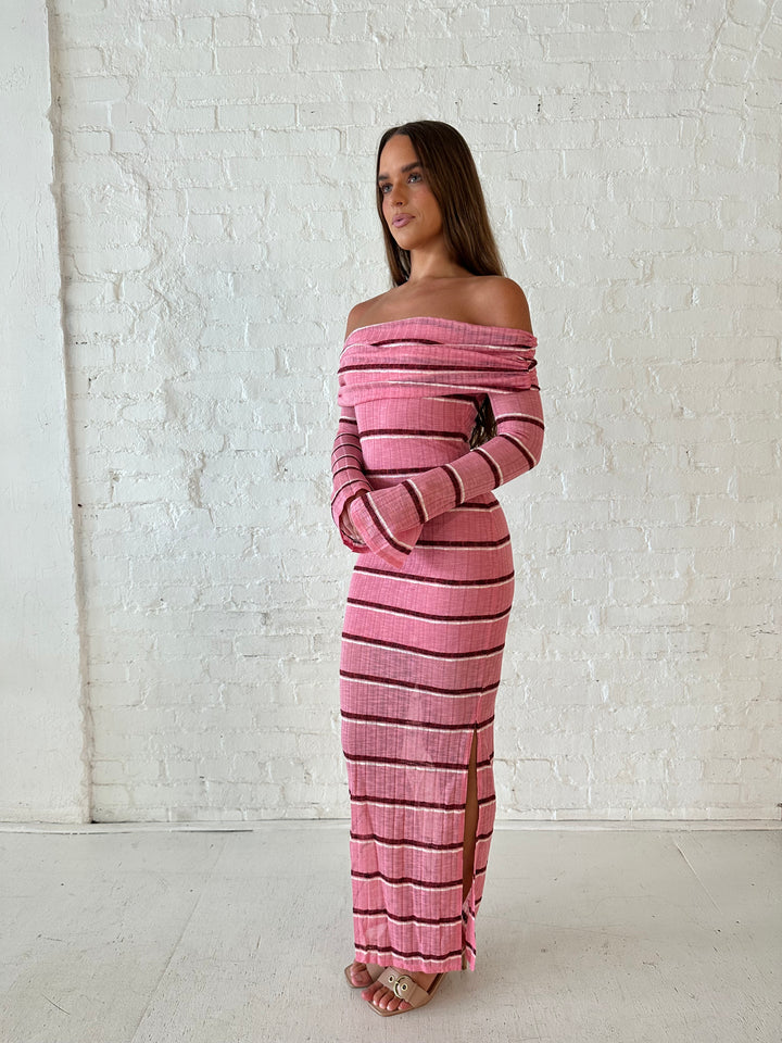 Woman wearing a pink maxi dress with burgundy stripes, fold over off the shoulder neckline, and long sleeves. 