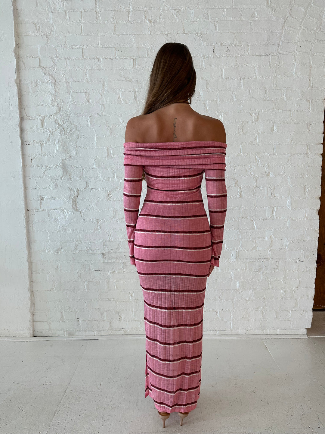 Woman wearing a pink maxi dress with burgundy stripes, fold over off the shoulder neckline, and long sleeves. 