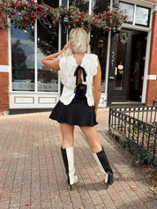 Woman wearing cream cable knit sweater with black bow detail
