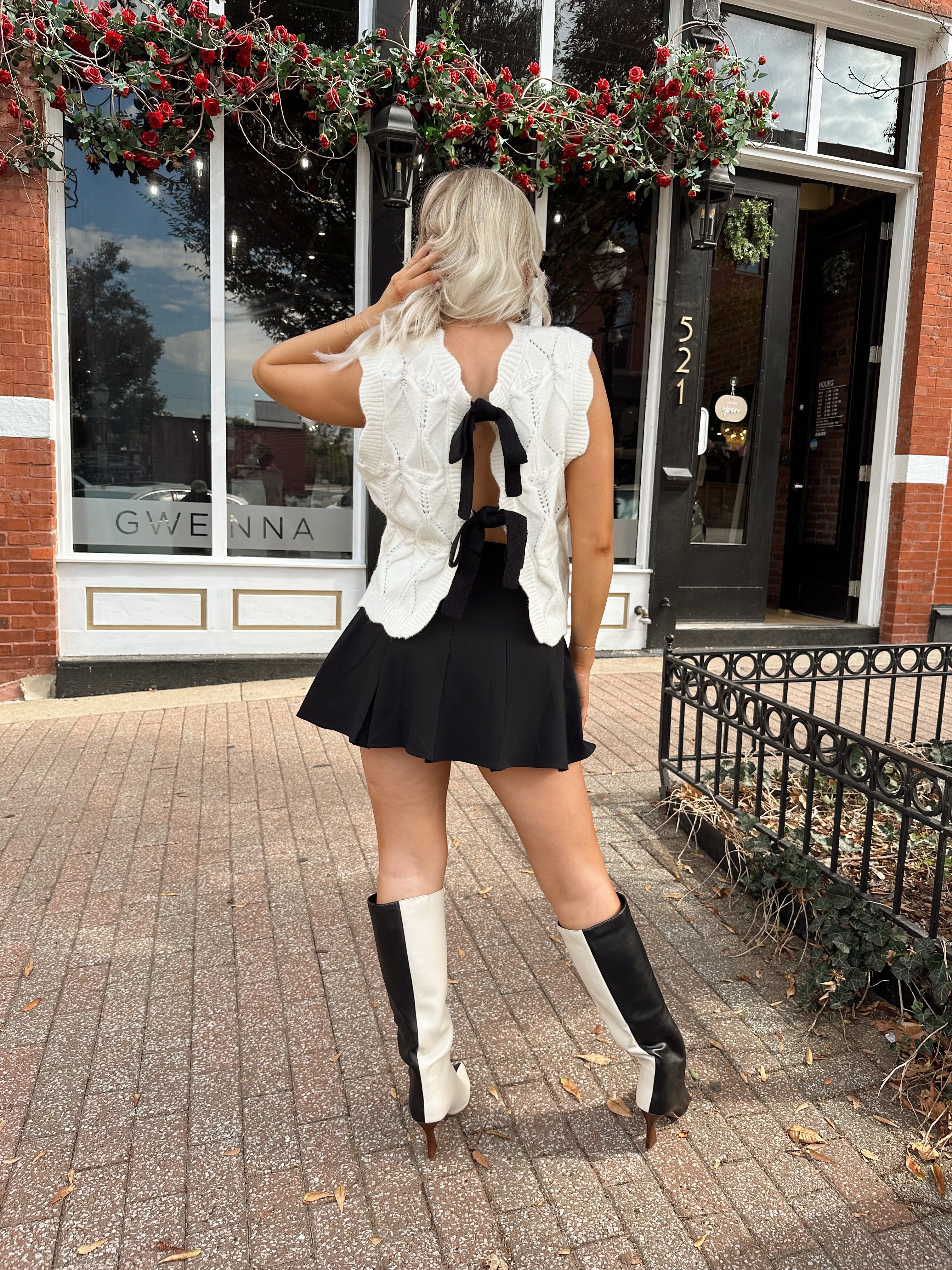 Woman wearing cream cable knit sweater with black bow detail
