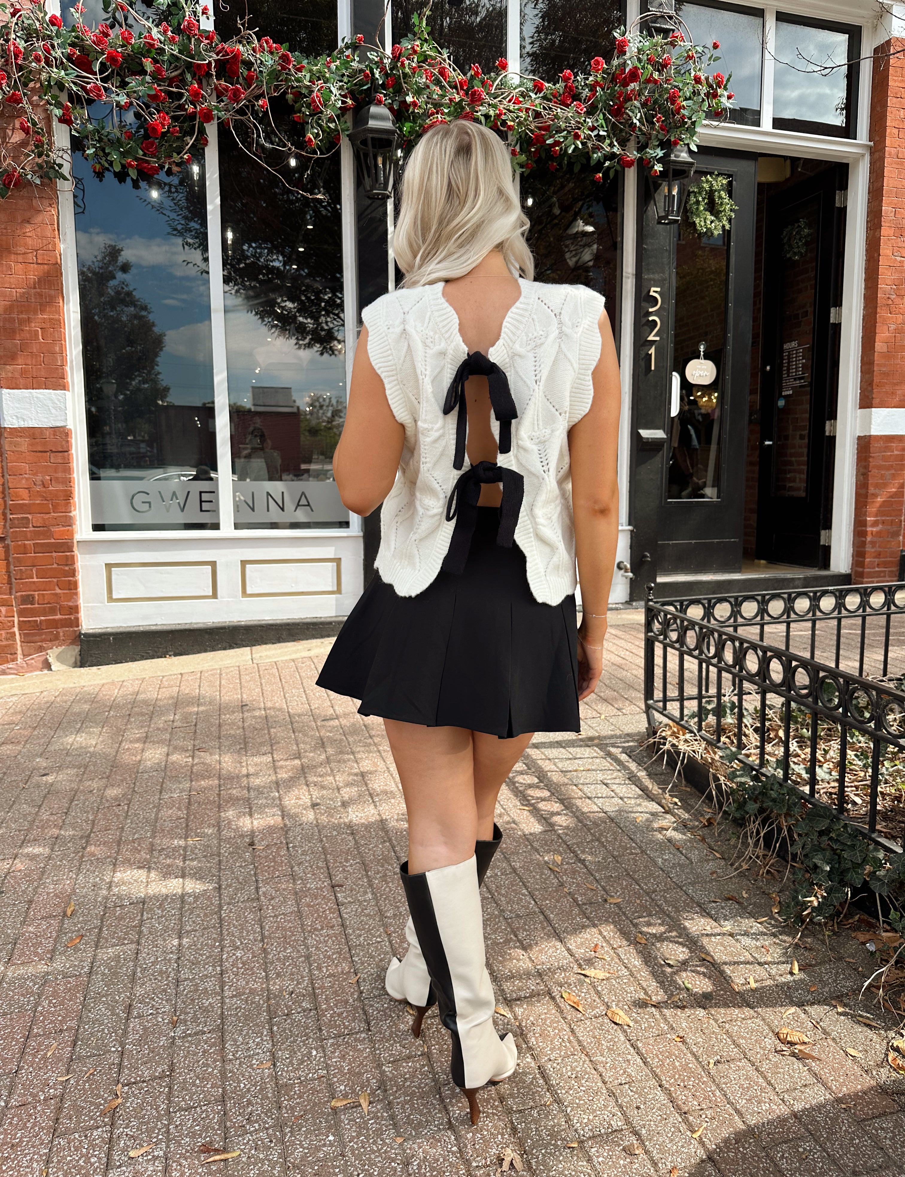 Woman wearing cream cable knit sweater with black bow detail