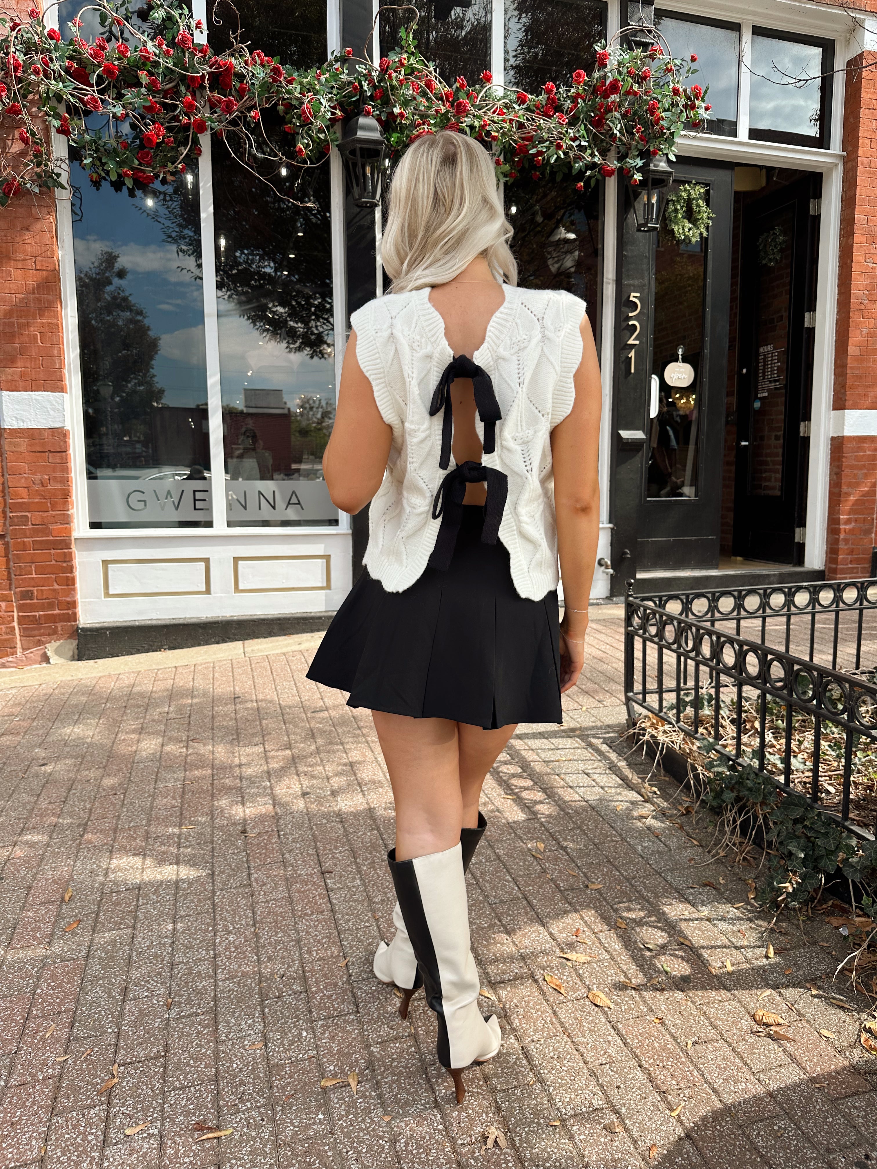 Woman wearing cream cable knit sweater with black bow detail