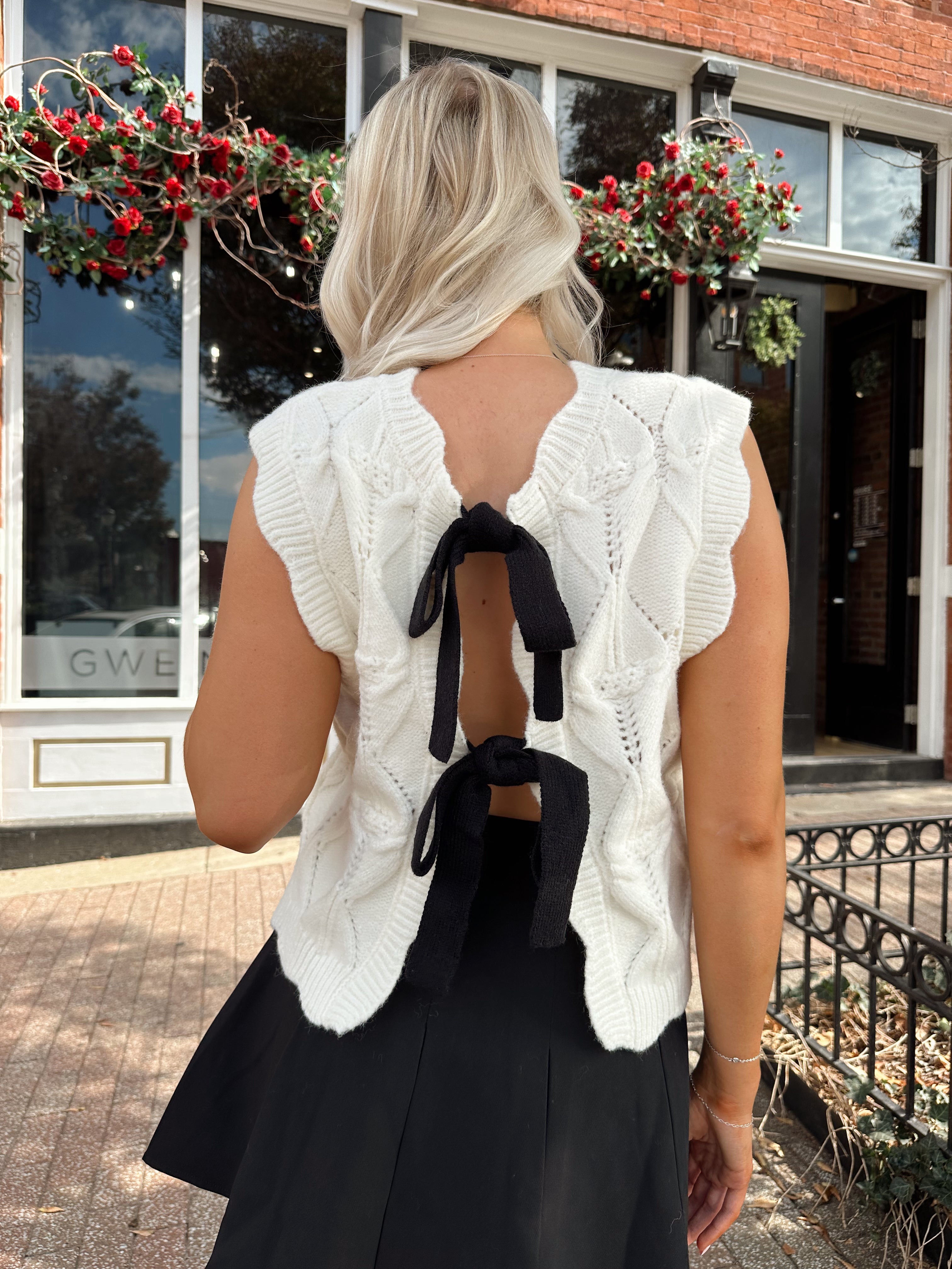 Woman wearing cream cable knit sweater with black bow detail.
