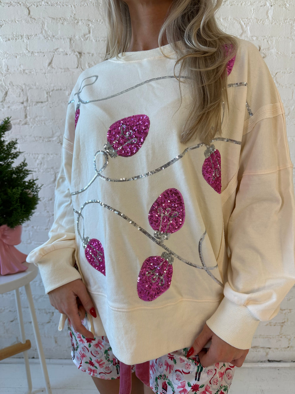 Woman wearing cream oversized crew neck with pink sequin string light across the front. 