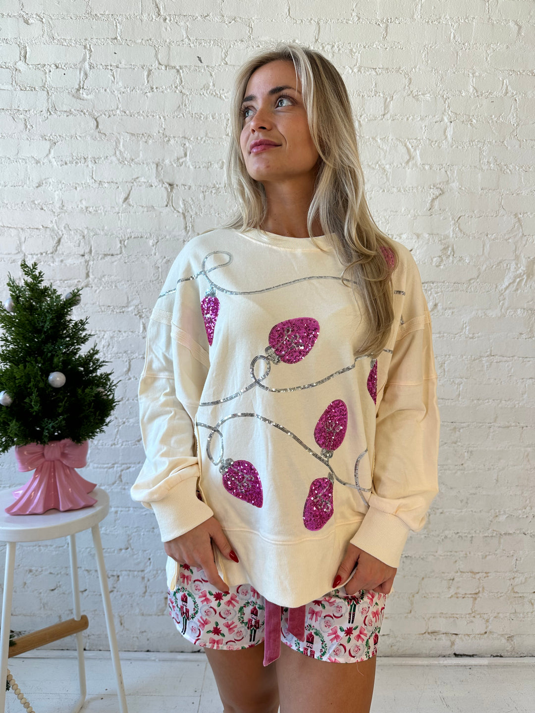 Woman wearing cream oversized crew neck with pink sequin string light across the front. 