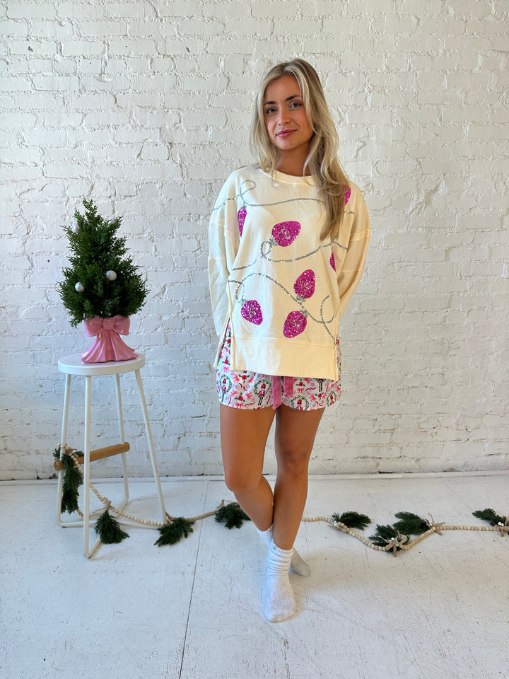 Woman wearing cream oversized crew neck with pink sequin string light across the front. 