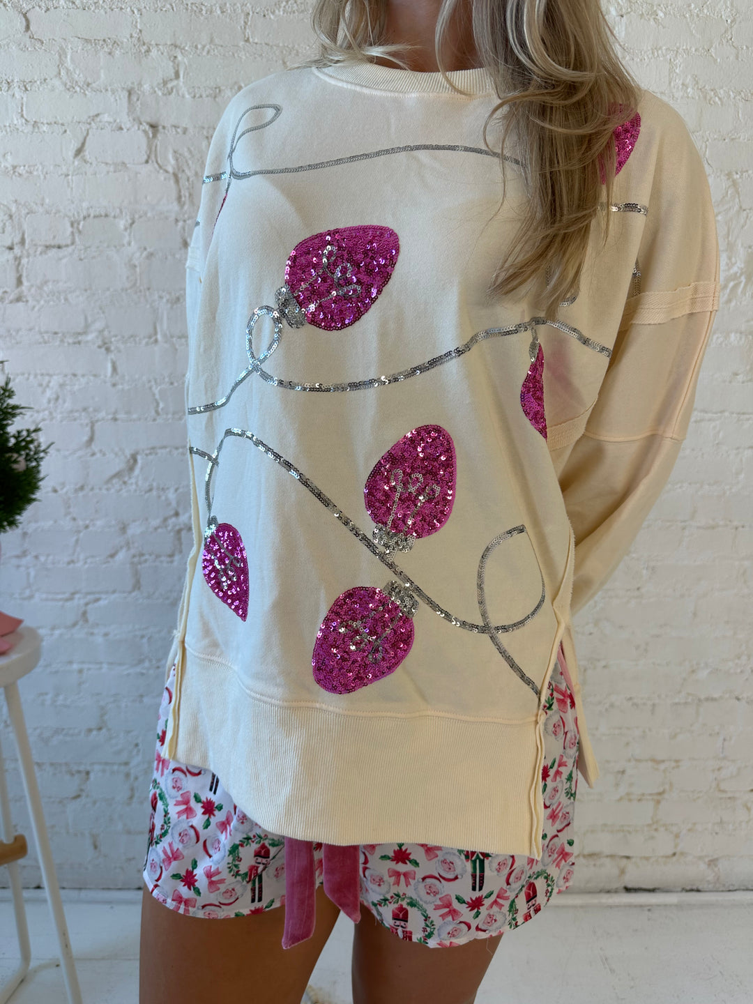 Woman wearing cream oversized crew neck with pink sequin string light across the front. 