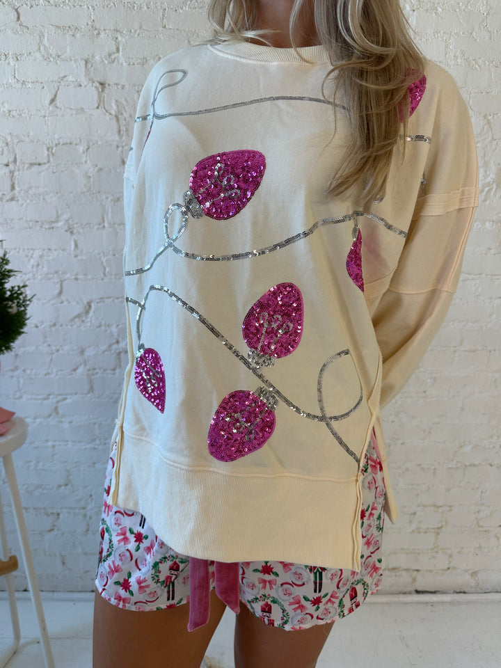 Woman wearing cream oversized crew neck with pink sequin string light across the front. 