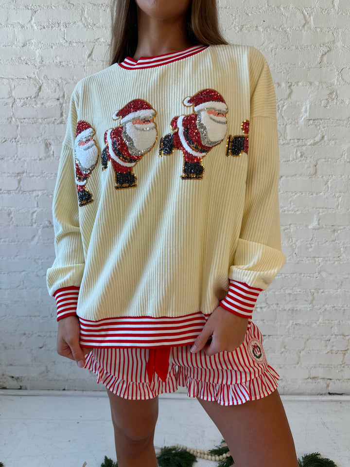 Woman wearing cream ribbed pull over with sequin santas skating on the front, and red striped trim. 