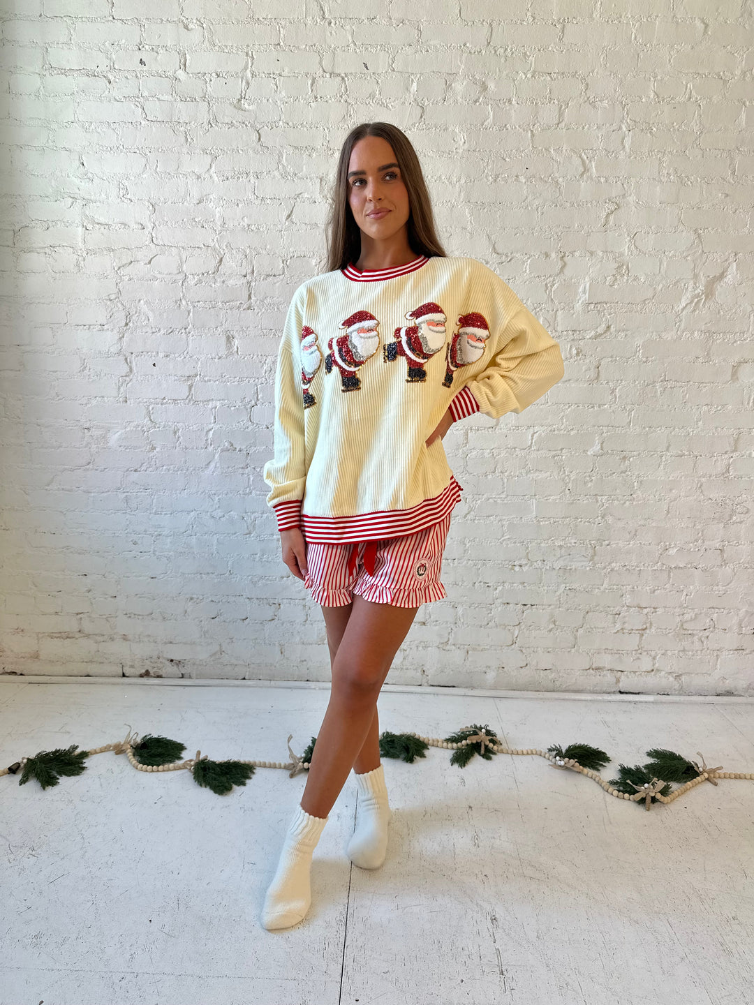 Woman wearing cream ribbed pull over with sequin santas skating on the front, and red striped trim. 