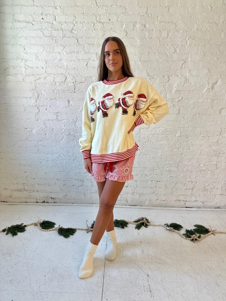 Woman wearing cream ribbed pull over with sequin santas skating on the front, and red striped trim. 