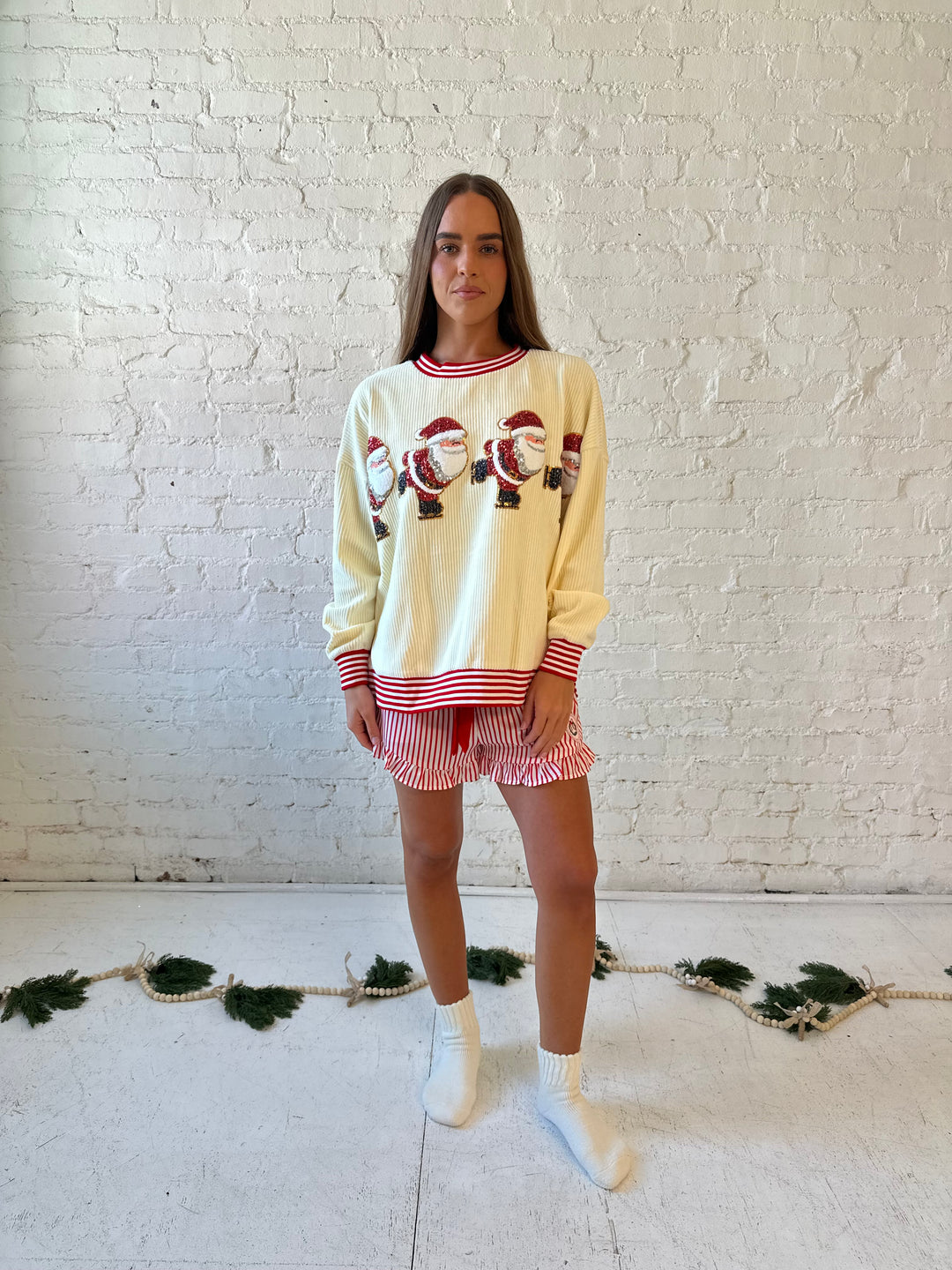 Woman wearing cream ribbed pull over with sequin santas skating on the front, and red striped trim. 