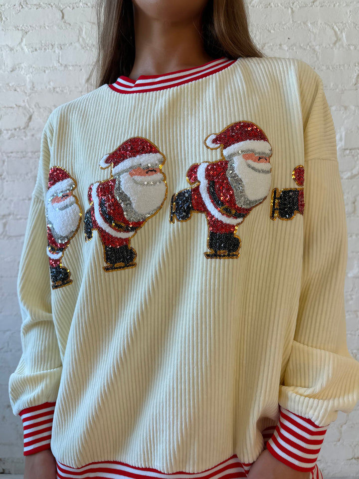 Woman wearing cream ribbed pull over with sequin santas skating on the front, and red striped trim. 