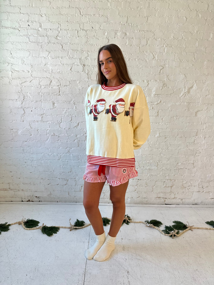 Woman wearing cream ribbed pull over with sequin santas skating on the front, and red striped trim. 