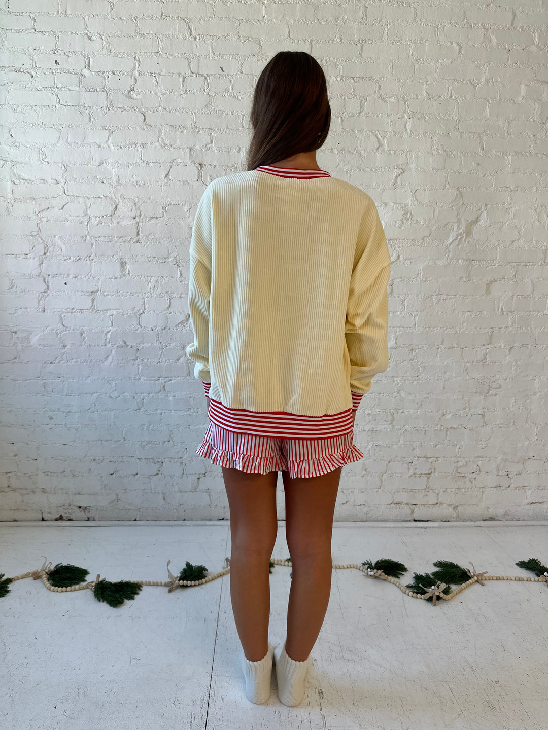 Woman wearing cream ribbed pull over with sequin santas skating on the front, and red striped trim. 
