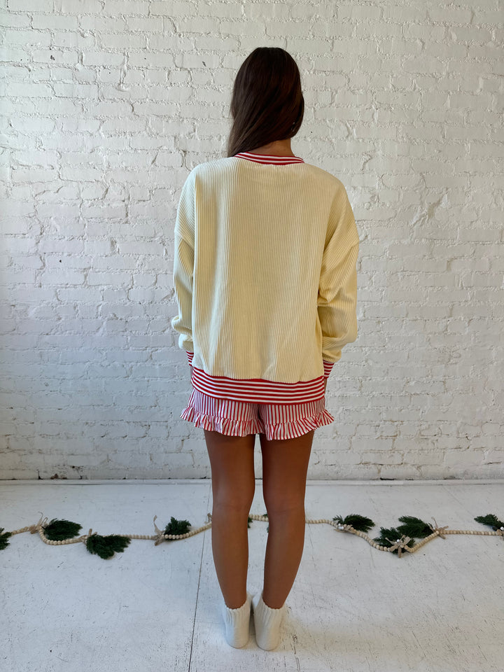 Woman wearing cream ribbed pull over with sequin santas skating on the front, and red striped trim. 