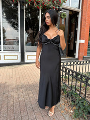 Woman wearing black satin maxi dress with white ruffle trim and open back. 