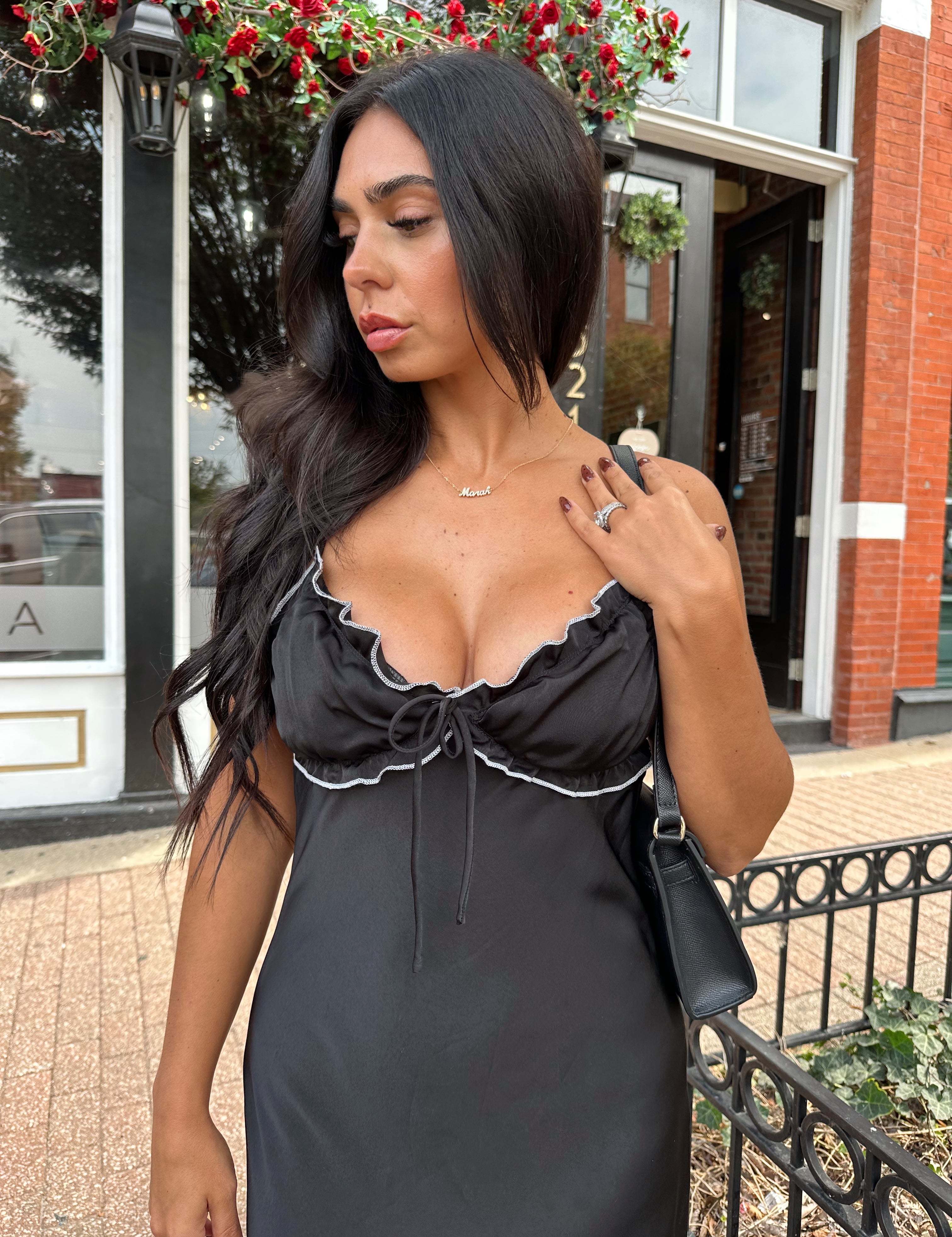 Woman wearing black satin maxi dress with white ruffle trim and open back. 