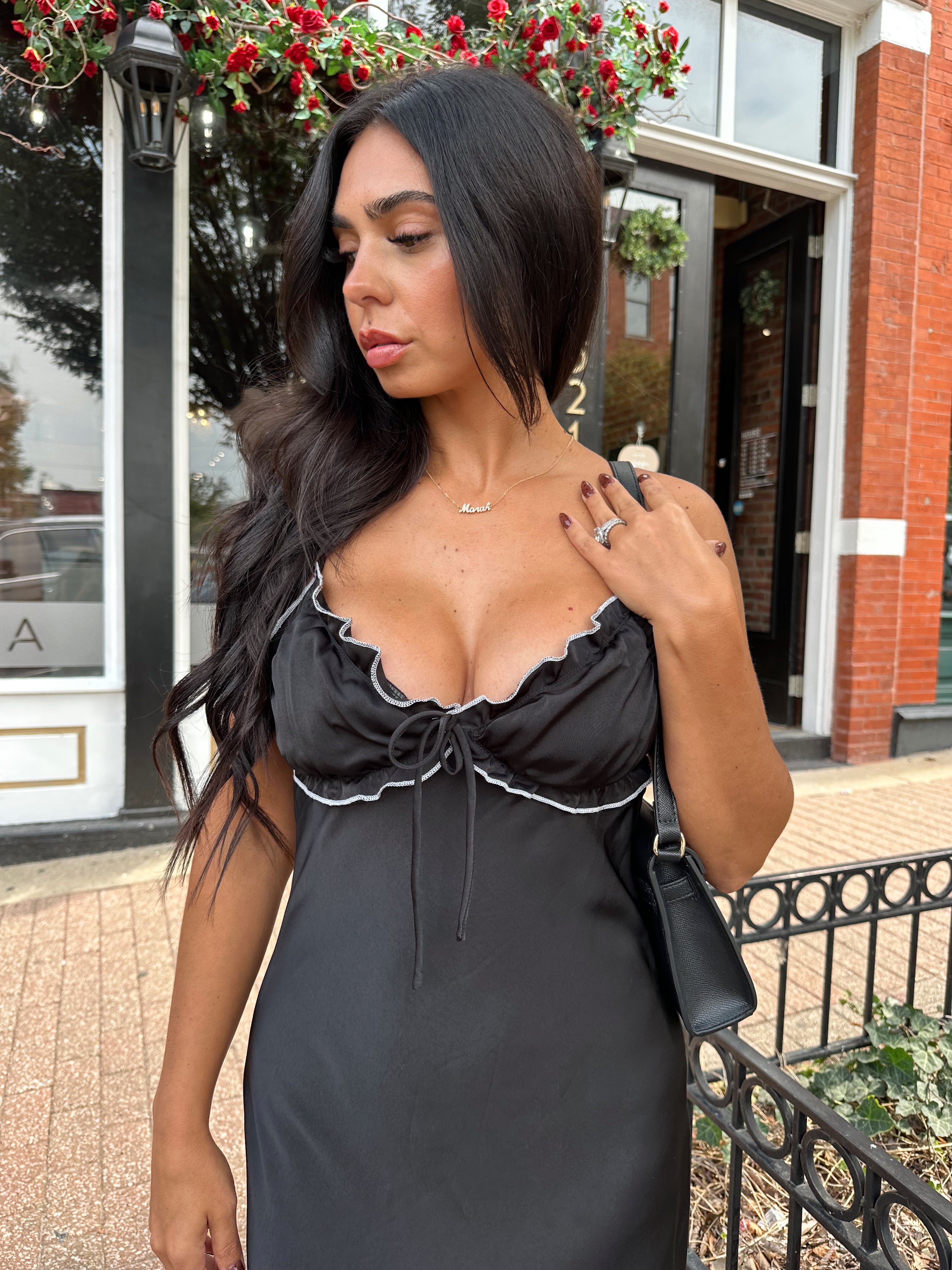 Woman wearing black satin maxi dress with white ruffle trim and open back. 