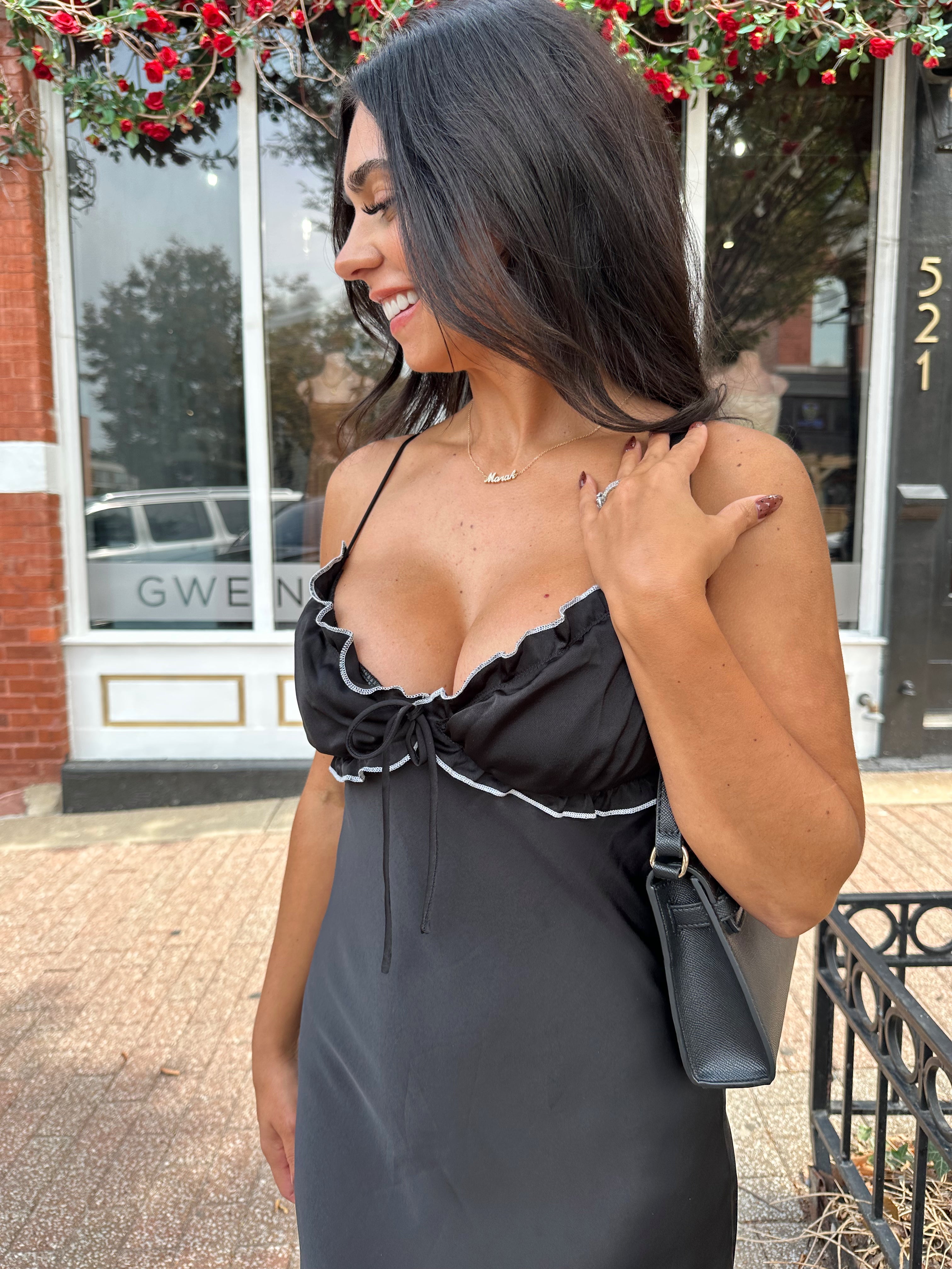 Woman wearing black satin maxi dress with white ruffle trim and open back. 