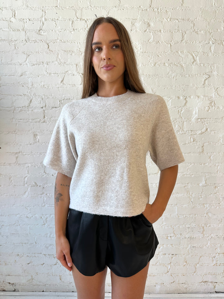 Woman wearing cream colored knit boxy fit tee shirt and faux leather short and heels. 