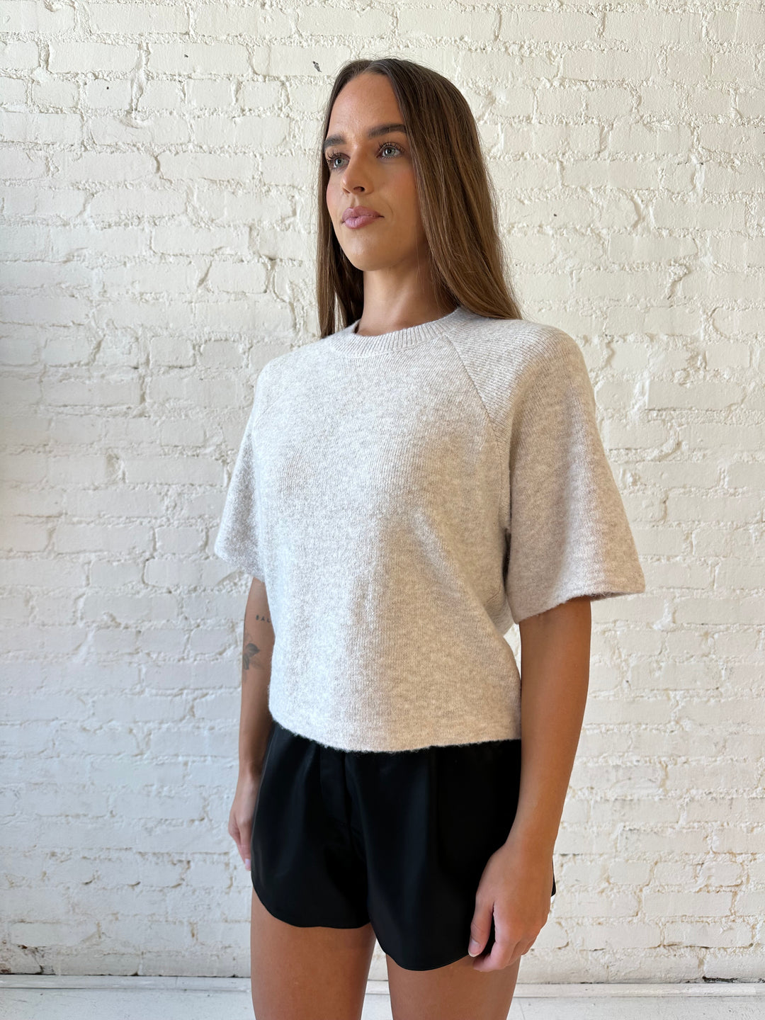 Woman wearing cream colored knit boxy fit tee shirt and faux leather short and heels. 