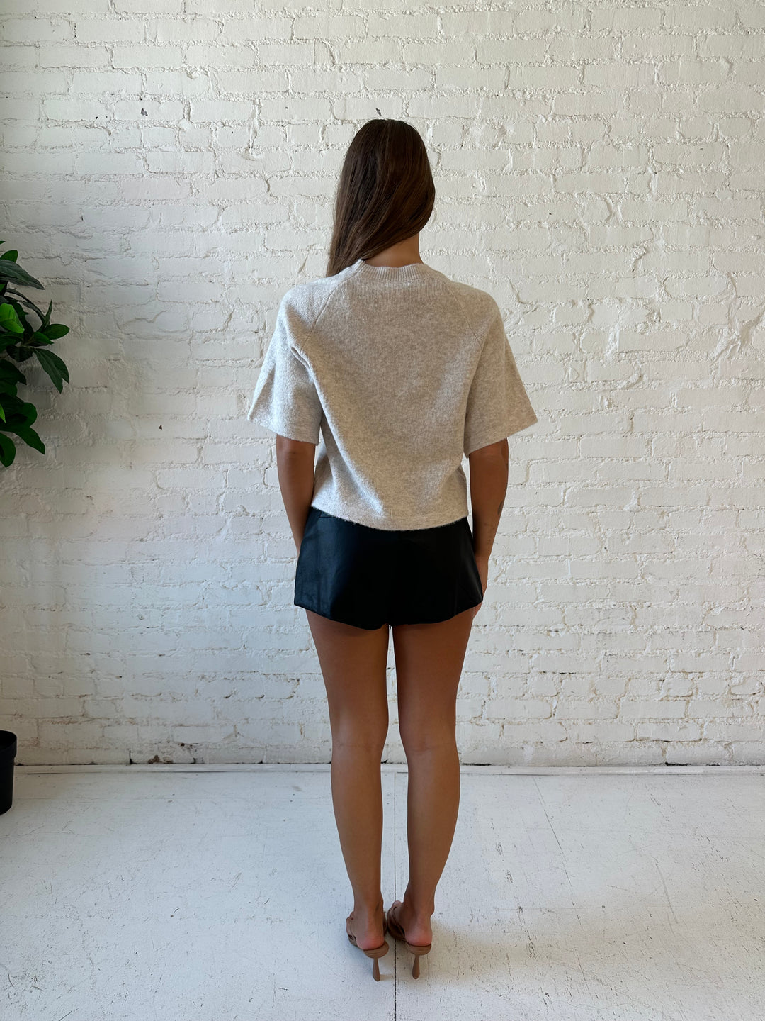 Woman wearing cream colored knit boxy fit tee shirt and faux leather short and heels. 