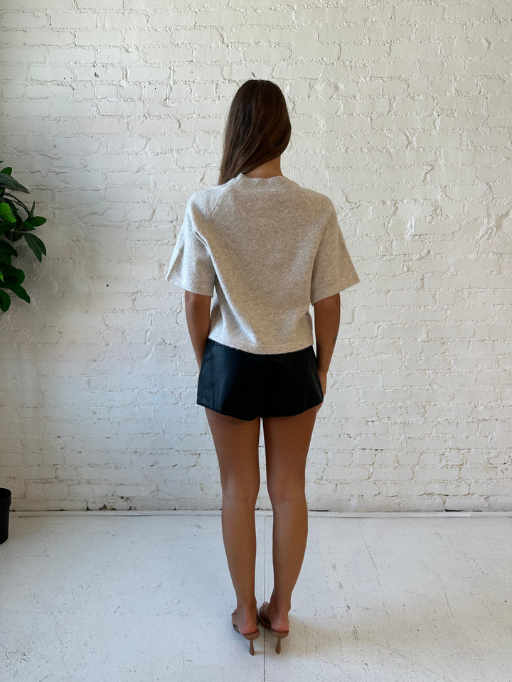 Woman wearing cream colored knit boxy fit tee shirt and faux leather short and heels. 