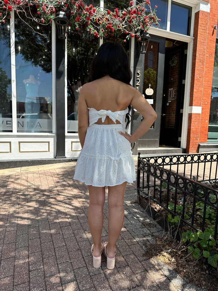 Woman wearing white strapless eyelet mini dress with tie back.