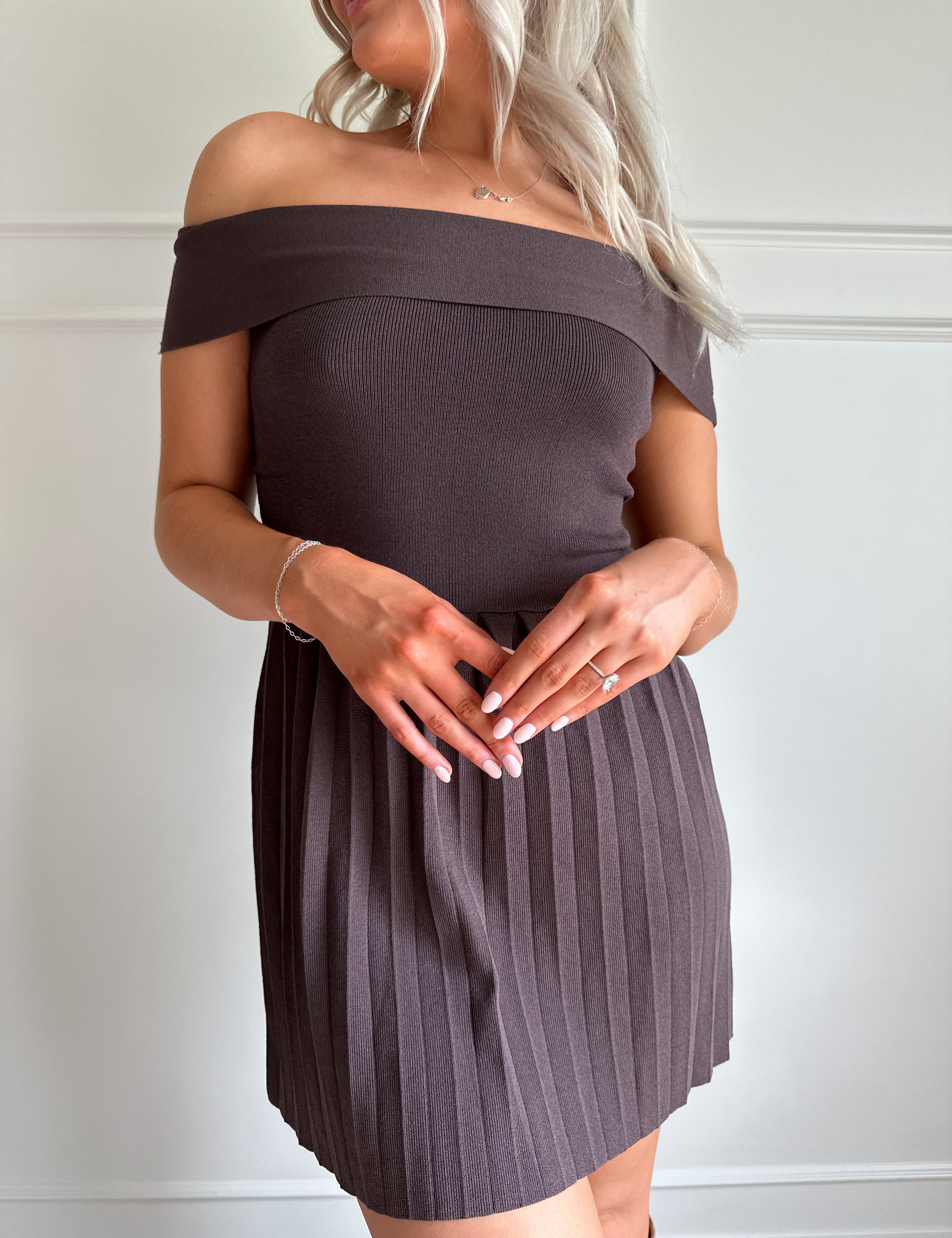 Woman wearing brown knit off the shoulder mini dress with pleated mini dress.