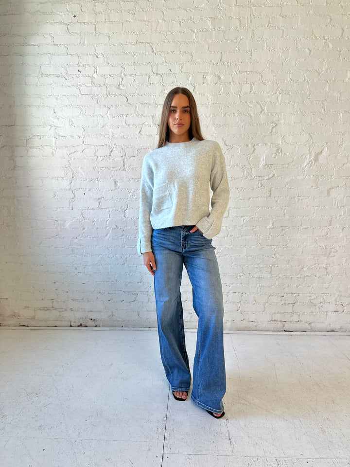 Woman wearing grey knit sweater with medium wash, wide leg jeans. 