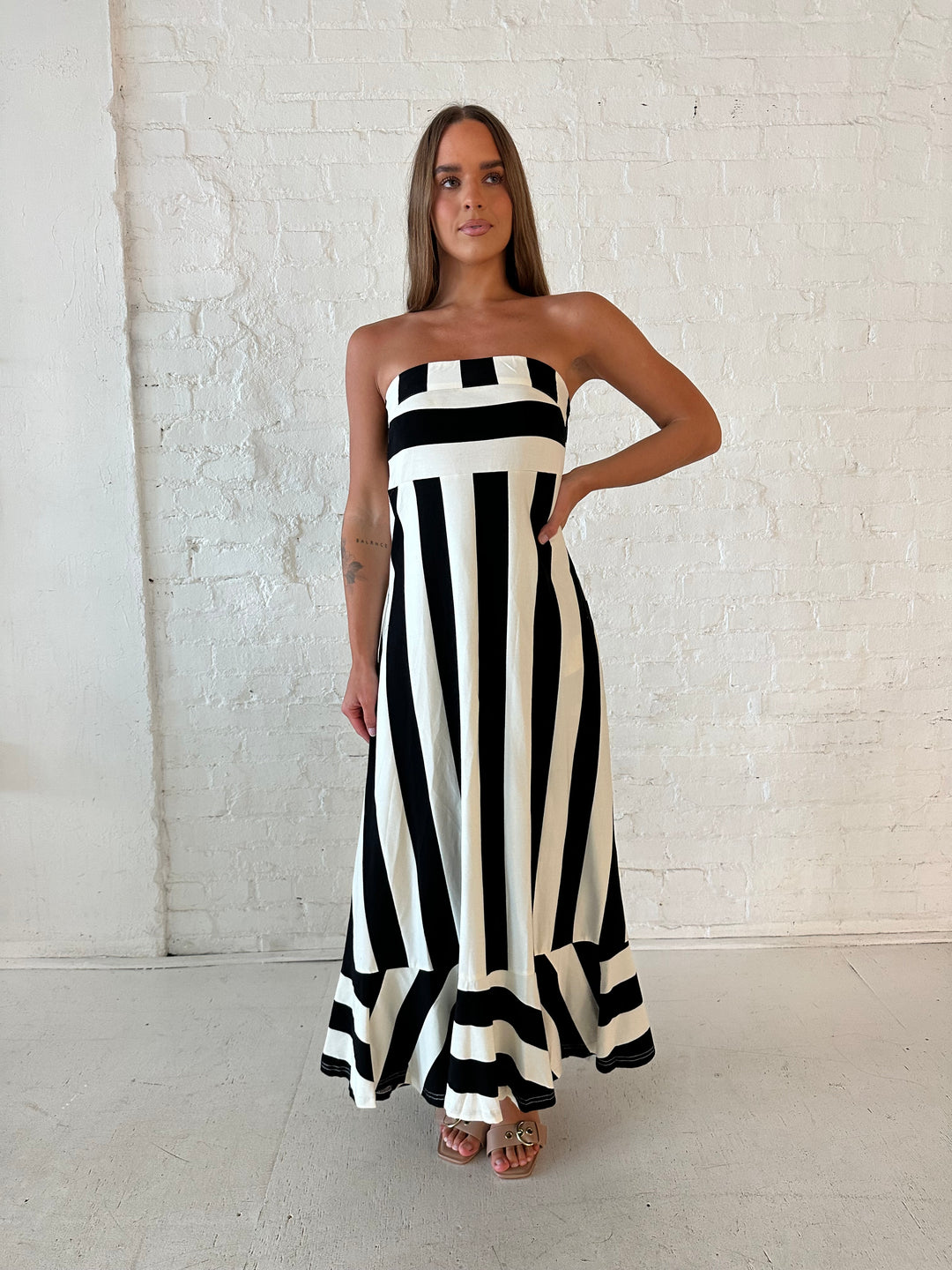 Woman wearing black and white striped, strapless midi dress with cutout back.