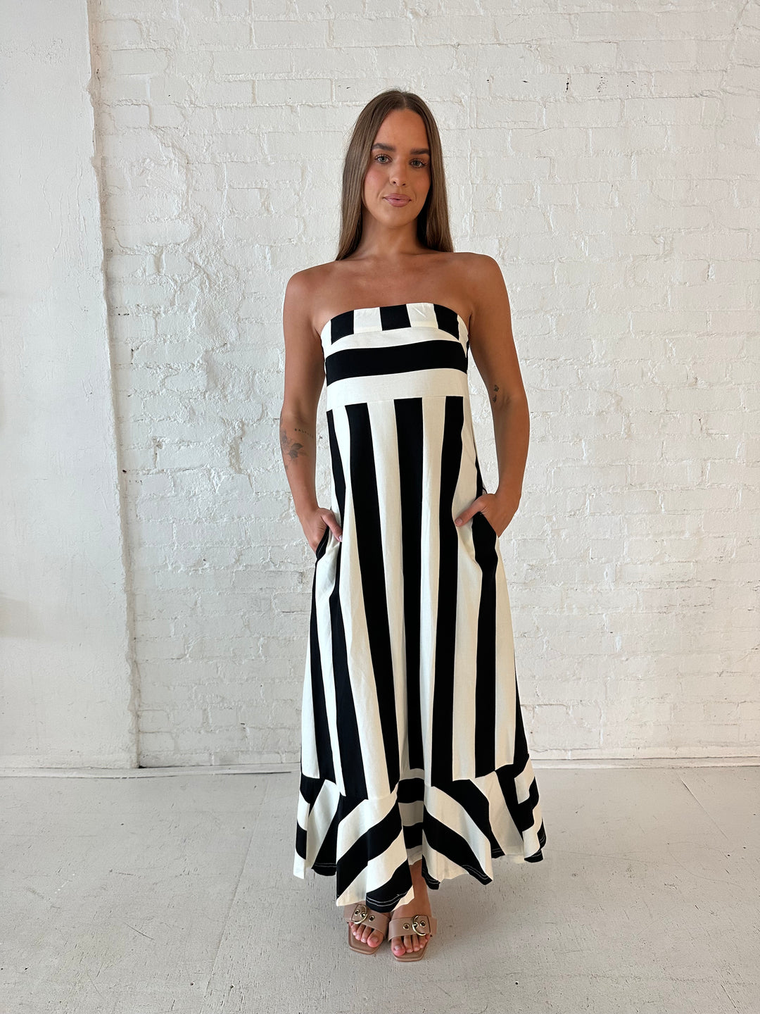 Woman wearing black and white striped, strapless midi dress with cutout back.