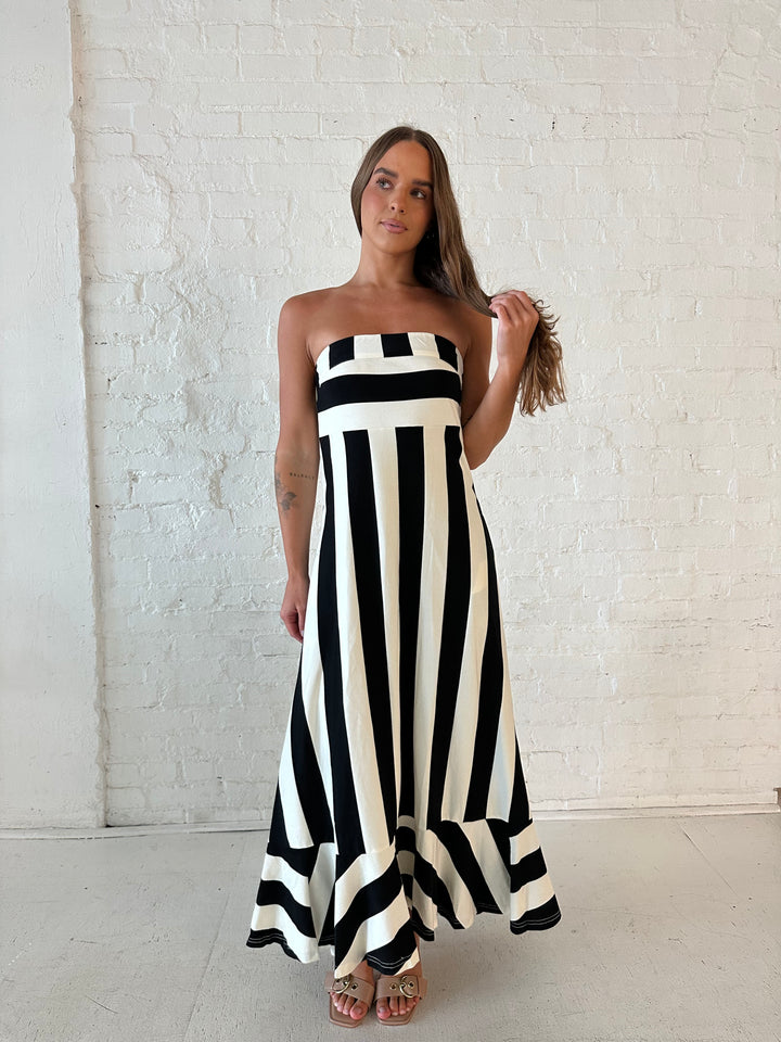 Woman wearing black and white striped, strapless midi dress with cutout back.