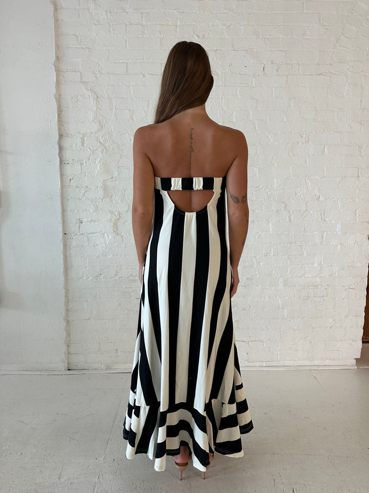 Woman wearing black and white striped, strapless midi dress with cutout back.