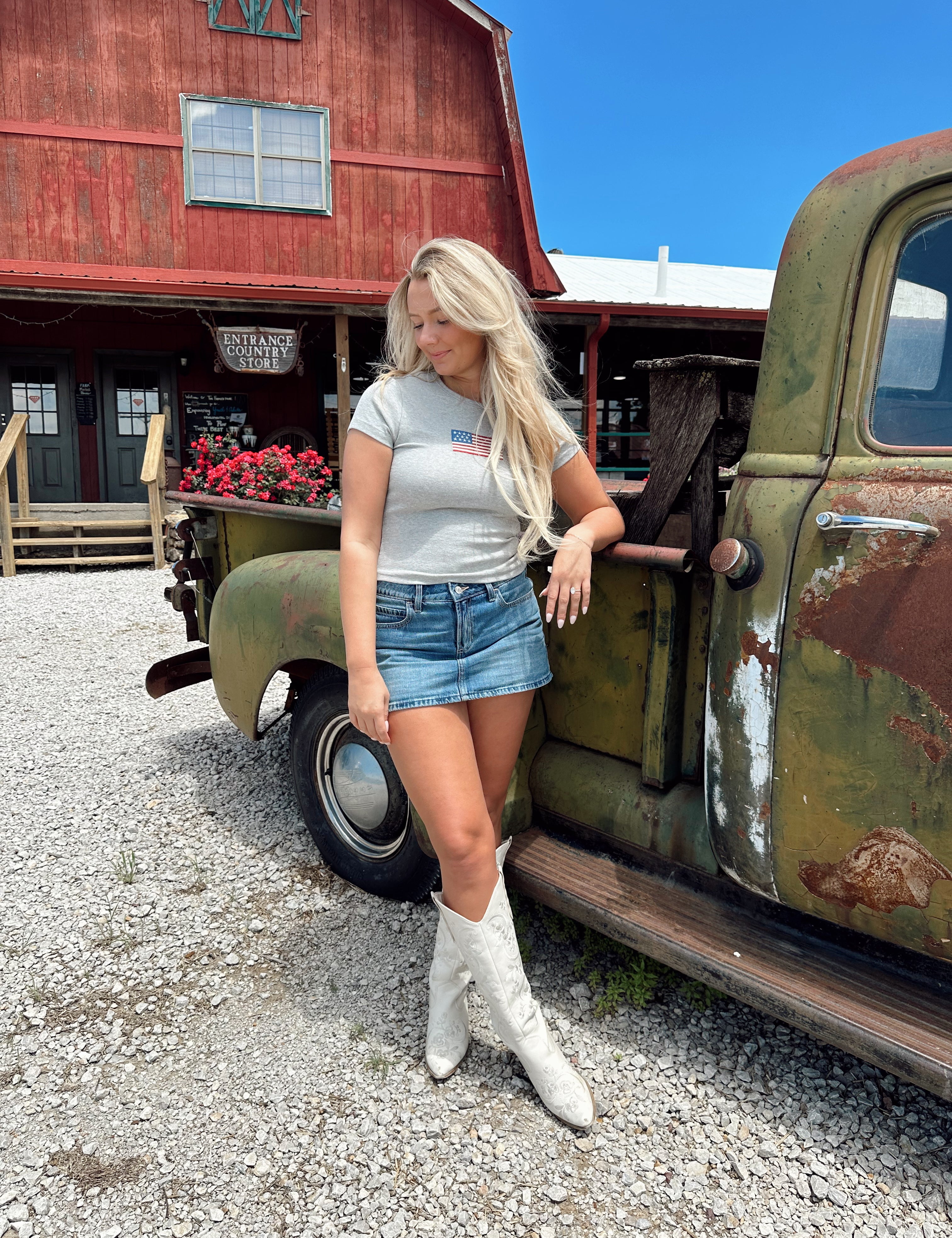 Woman in a dark grey baby tee with an embroidered American flag, paired with a denim mini skirt