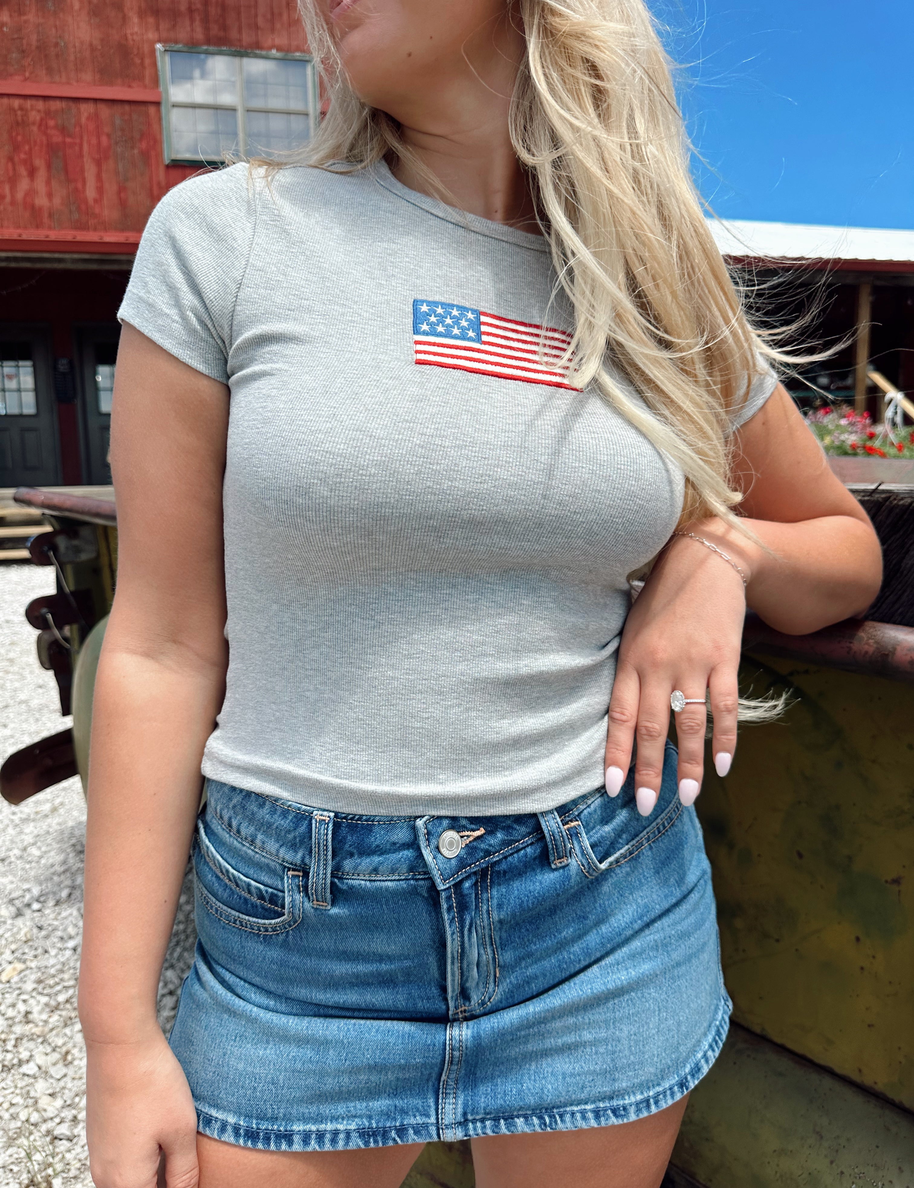 Woman in a dark grey baby tee with an embroidered American flag, paired with a denim mini skirt