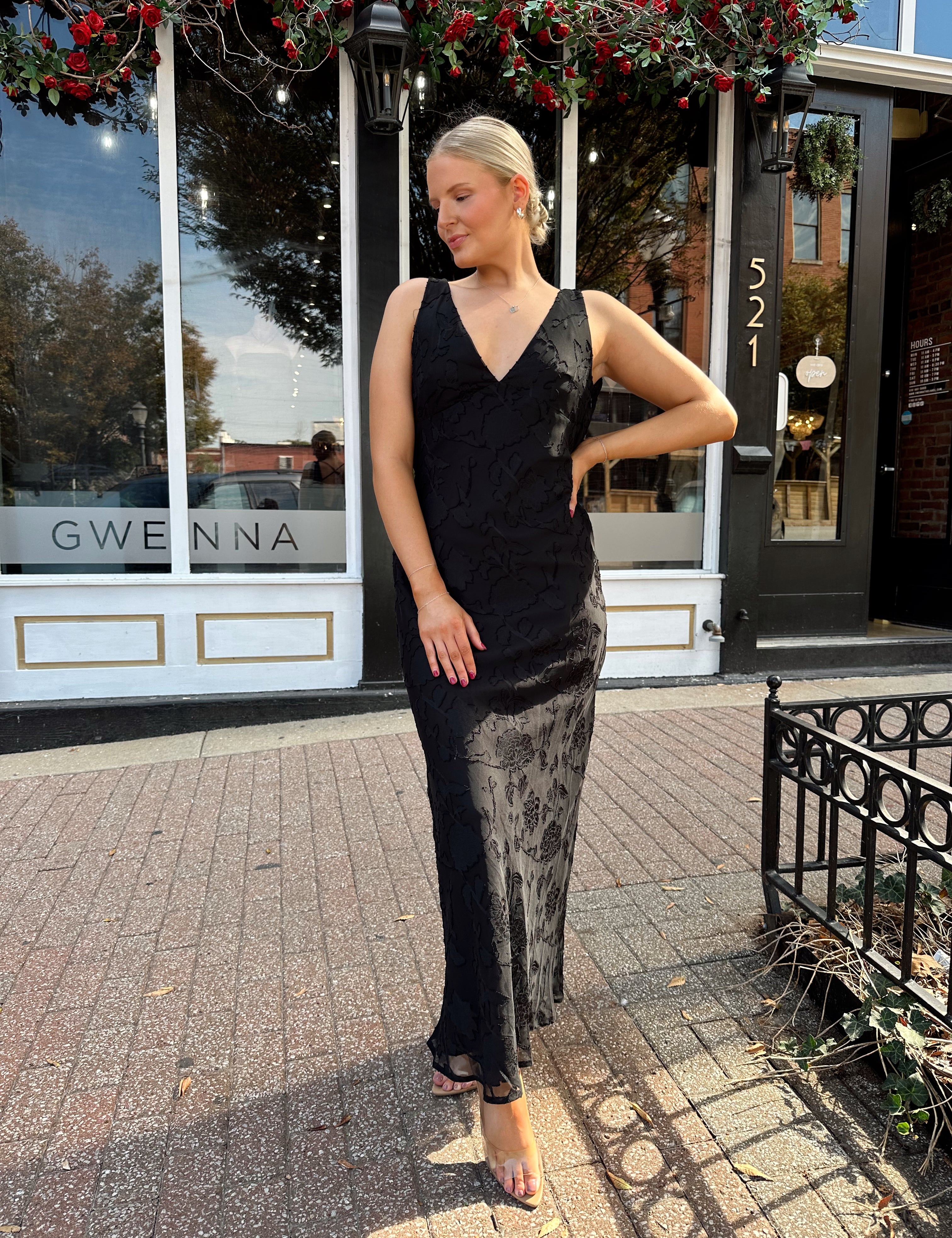 Woman wearing black textured midi dress with criss-cross cowl back. 