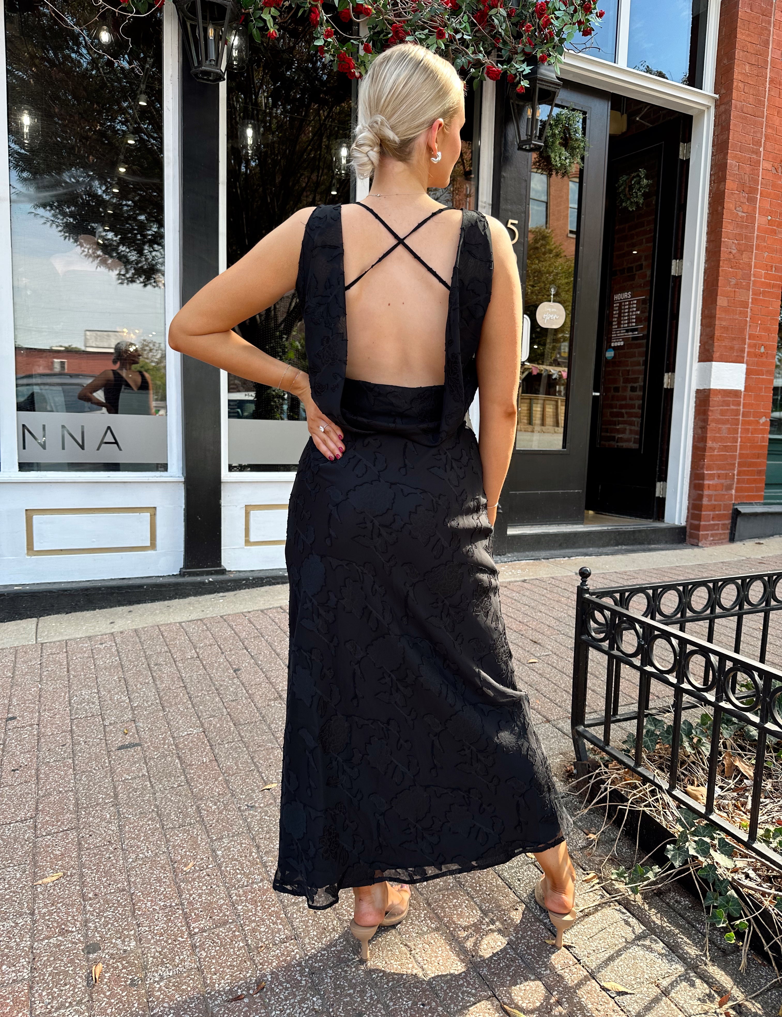 Woman wearing black textured midi dress with criss-cross cowl back. 