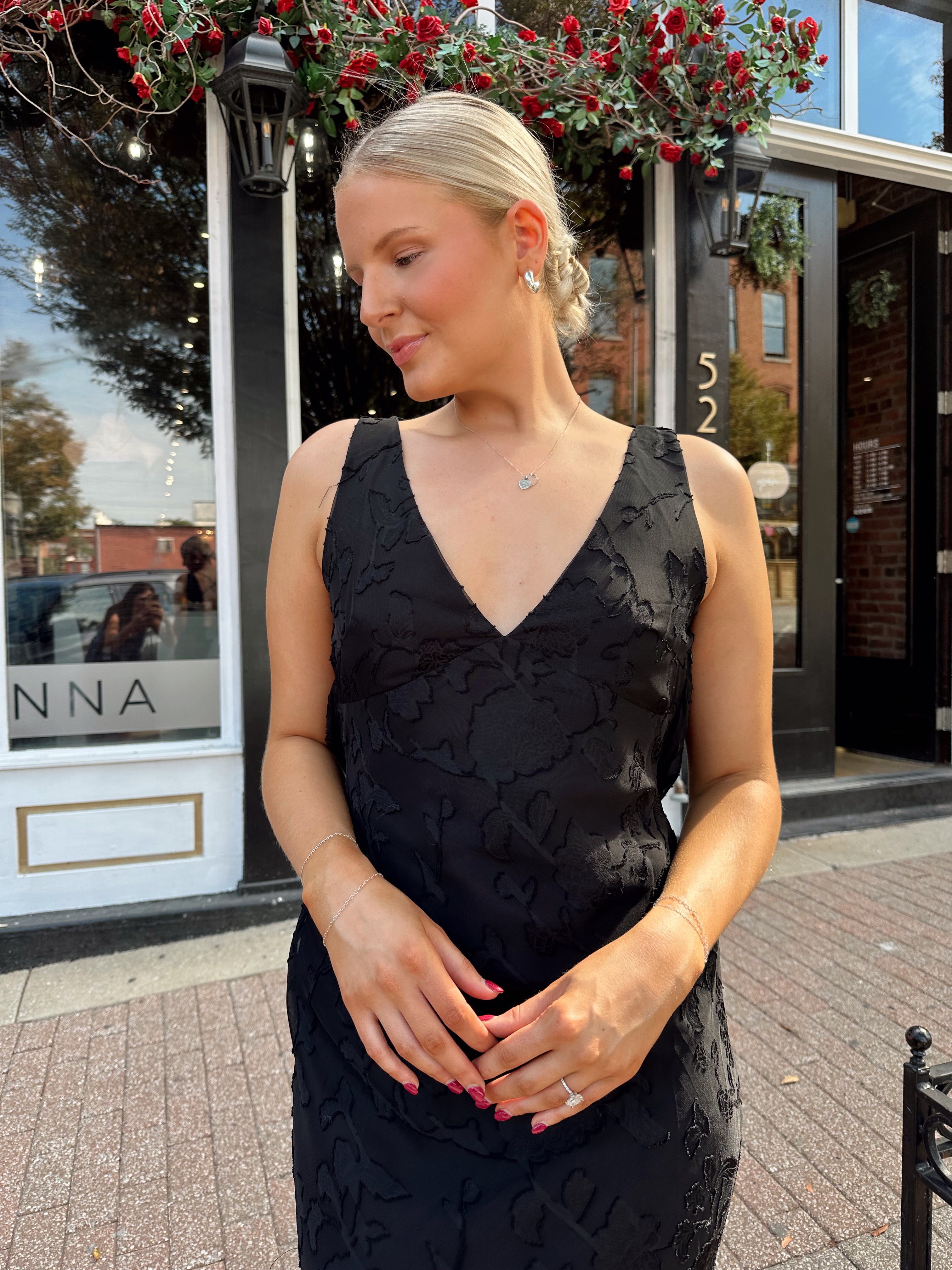 Woman wearing black textured midi dress with criss-cross cowl back. 