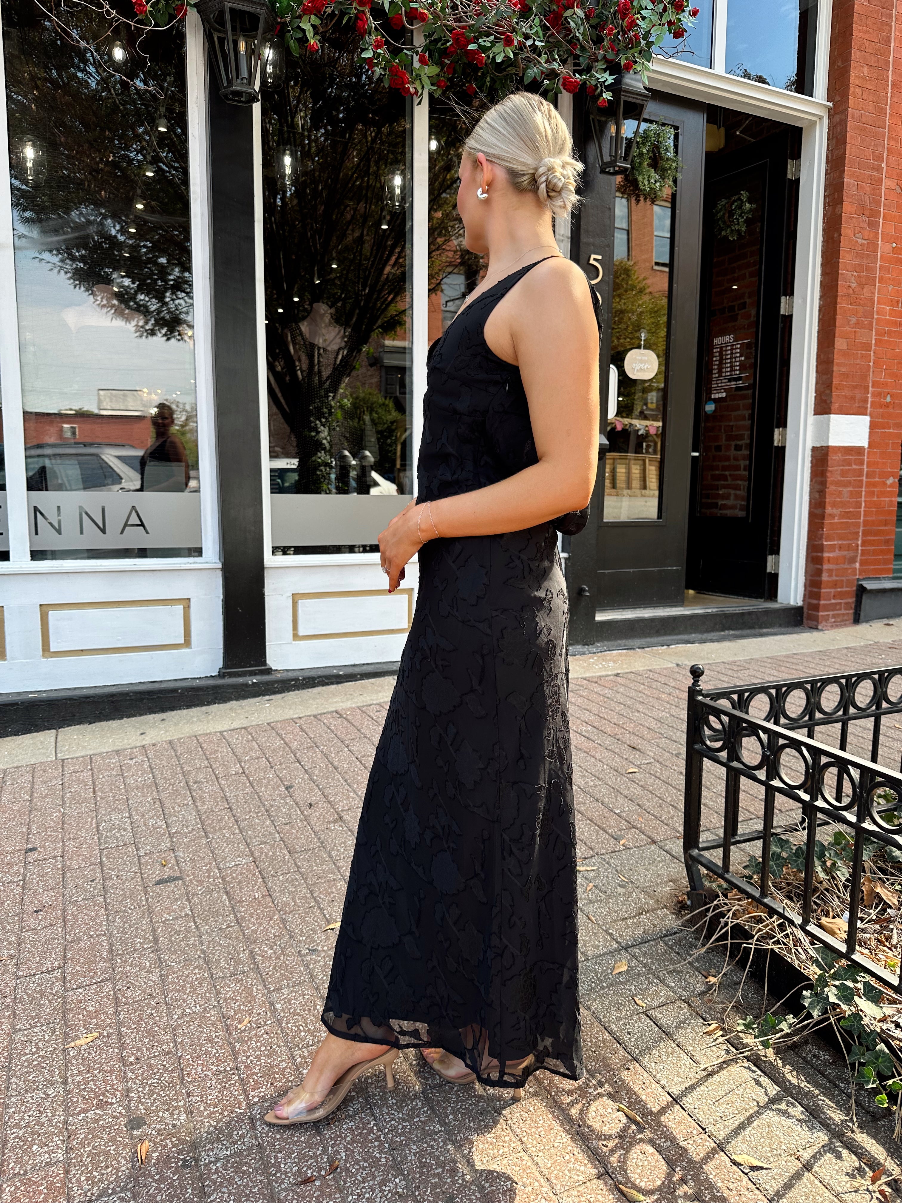Woman wearing black textured midi dress with criss-cross cowl back. 