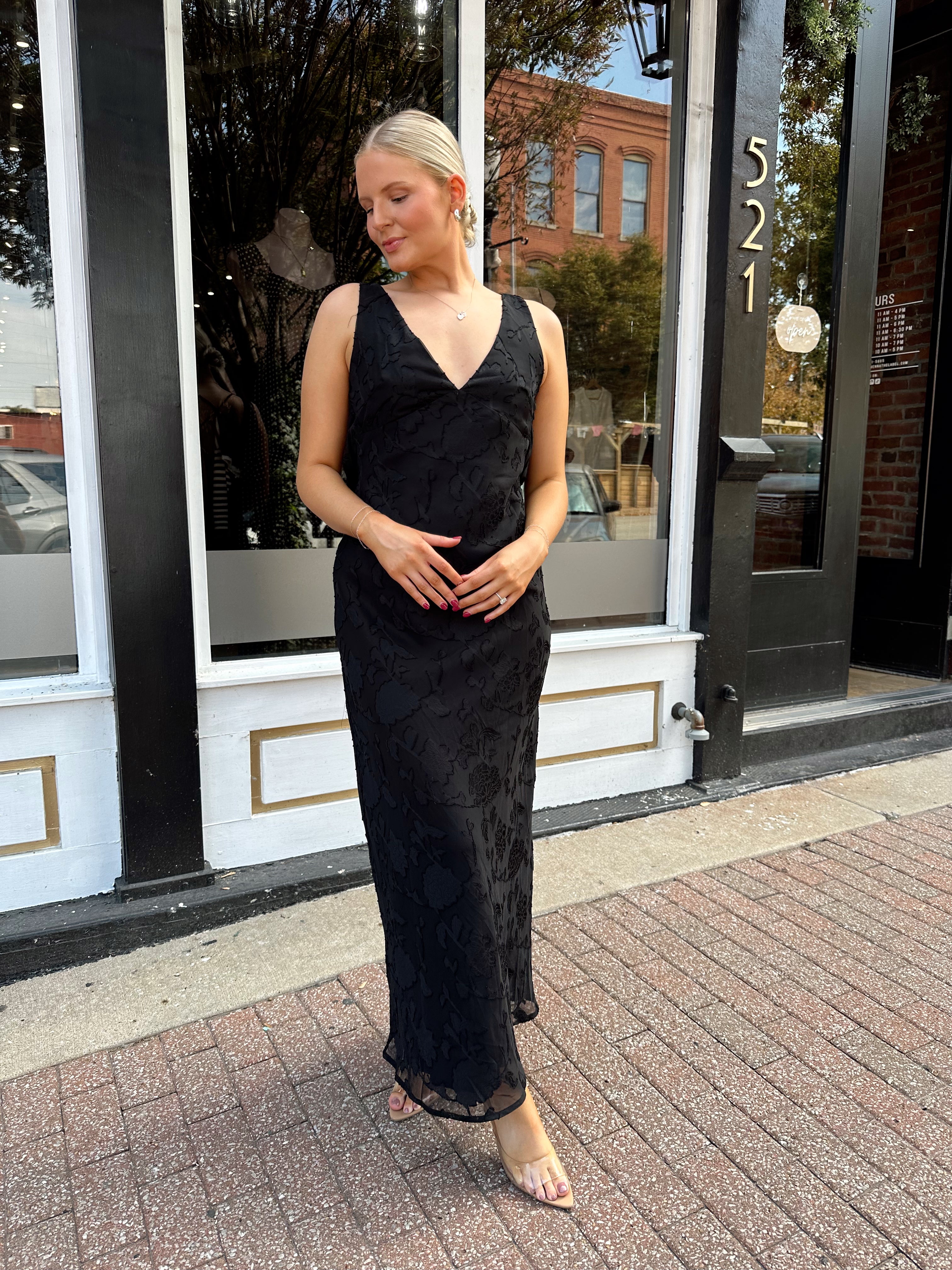 Woman wearing black textured midi dress with criss-cross cowl back. 