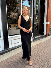 Woman wearing black textured midi dress with criss-cross cowl back. 